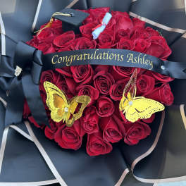 Red rose bouquet with a graduation cap and black ribbon reading Congratulations Ashley