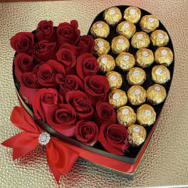 Heart-shaped box filled with red roses and gold-wrapped chocolates, tied with a red bow.