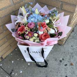 Mixed bouquet with pink roses, blue hydrangea, and white lilies in pink wrap