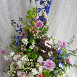 Tall floral arrangement with blue and pink flowers and a metallic angel figure