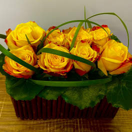 Yellow roses in a red basket with green decorative loops