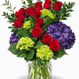 Red roses and purple hydrangeas in a clear glass vase