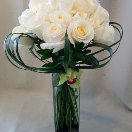 White rose bouquet in a tall glass vase with looping green leaves