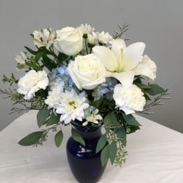 White roses, lilies, and daisies in a dark blue vase