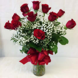 Red roses arranged in a glass vase with baby's breath and a red ribbon