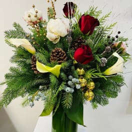 Tall holiday arrangement with red roses, white blooms, calla lilies, evergreens, pinecones and gold ornaments in a green vase