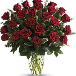 Large arrangement of dark red roses with eucalyptus in a clear glass vase.
