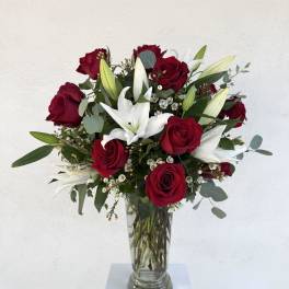 Tall arrangement of red roses and white lilies in a clear glass vase