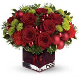 Low red and green arrangement with roses, mums, and ornaments in a red glass cube vase
