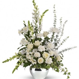 White floral arrangement with roses, snapdragons, and mums in a round silver vase with trailing ivy.