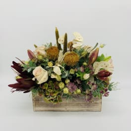 Low centerpiece of cream roses, golden protea, and mixed blooms in a rustic wooden box