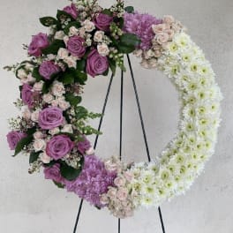 Large open wreath of purple and white flowers displayed on a black metal easel