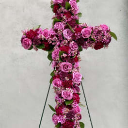 Standing floral cross of pink and burgundy blooms on a metal easel.