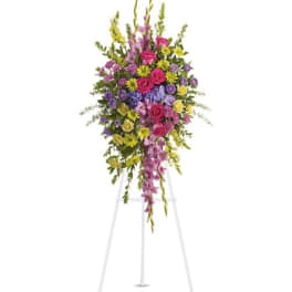 Bright standing spray of pink roses and mixed yellow and purple flowers on a white easel.