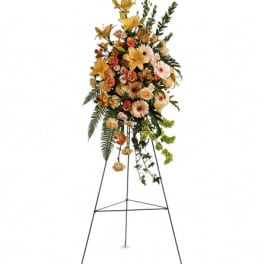 Tall standing spray of yellow lilies, peach roses, and gerberas on a metal easel