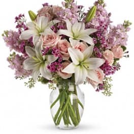 Pink roses, white lilies, and purple flowers arranged in a clear glass vase