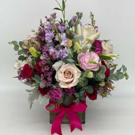 Mixed pink, red, and cream flower arrangement in a wooden cube with a bright pink bow.