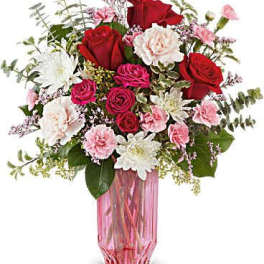 Bouquet of red and pink roses with white daisies in a pink glass vase