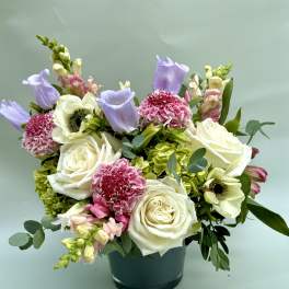 Mixed bouquet of white roses, pink carnations, and lavender blooms in a dark vase