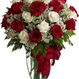 Red and white roses in a clear glass vase with a red ribbon