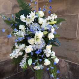 Tall standing spray of white lilies and roses with blue flowers on an easel