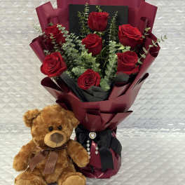 Bouquet of red roses with a teddy bear beside it