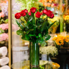 Tall arrangement of red roses in a clear glass vase on a reflective table