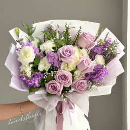 Hand-tied bouquet of lavender roses and purple-white blooms wrapped in pastel paper