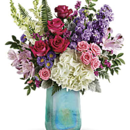Mixed bouquet of roses, hydrangeas, and purple flowers in a blue vase