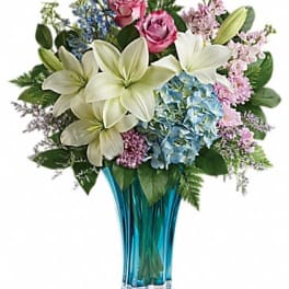 Bouquet of white lilies, pink roses, and blue hydrangeas in a blue glass vase