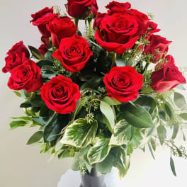 Arrangement of red roses with variegated foliage in a tall dark glass vase