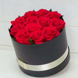 Round black box filled with red roses and wrapped with a cream ribbon