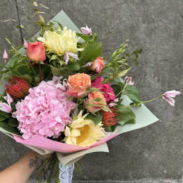 Handheld bouquet of pink, peach, and cream flowers wrapped in pastel paper