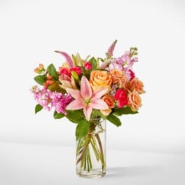 Mixed bouquet of pink lilies, roses, and orchids in a clear glass vase