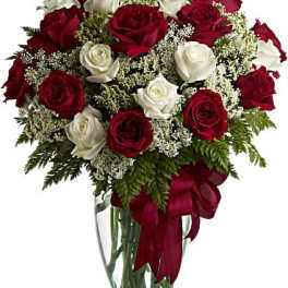 Arrangement of red and white roses in a clear glass vase with a red ribbon bow.