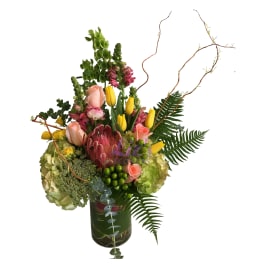 Mixed bouquet with pink roses, yellow tulips, and a protea in a glass vase