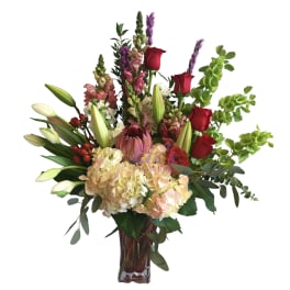 Tall bouquet of red roses, lilies, and hydrangeas in a glass vase