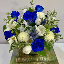 Blue and white flower arrangement in a glass vase on stacked decorative boxes
