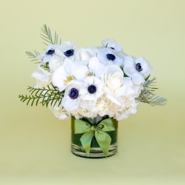 White floral arrangement in a glass vase with a green ribbon