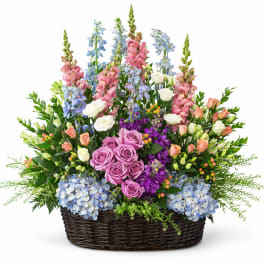 Large basket arrangement of roses, hydrangeas, and tall blue and pink blooms