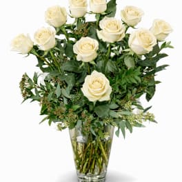 White roses arranged in a clear glass vase with greenery