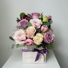 Pink and lavender roses arranged in a square box with a purple ribbon