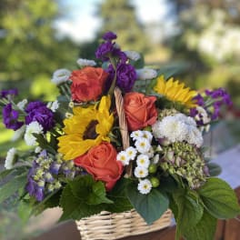 Basket arrangement with orange roses, sunflowers, and purple blooms