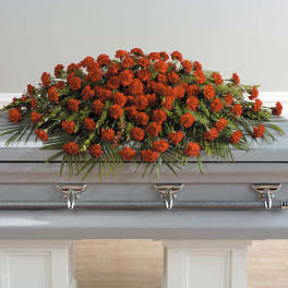 Orange floral casket spray with greenery on a gray coffin