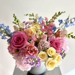 Mixed bouquet of pink, yellow, and blue flowers in a white vase