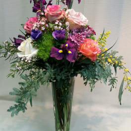 Tall mixed bouquet of roses, irises, and purple flowers in a clear glass vase