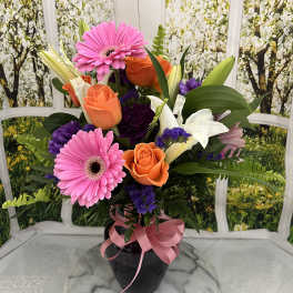 Bouquet of pink gerbera daisies, orange roses, and white lilies in a black vase