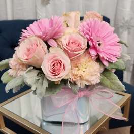 Pink roses and gerbera daisies in a clear glass vase with a pink ribbon