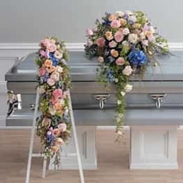 Pastel flower casket spray with matching cascading arrangement beside a silver casket