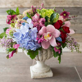 Mixed bouquet of pink, blue, red, and green flowers in a white pedestal vase